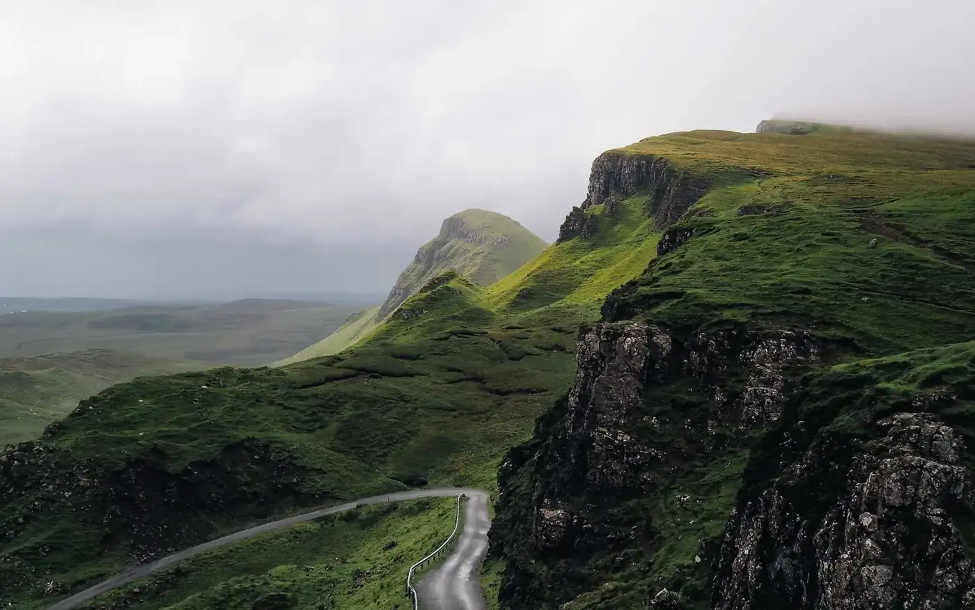A single track road winding between steep green hills under low cloud